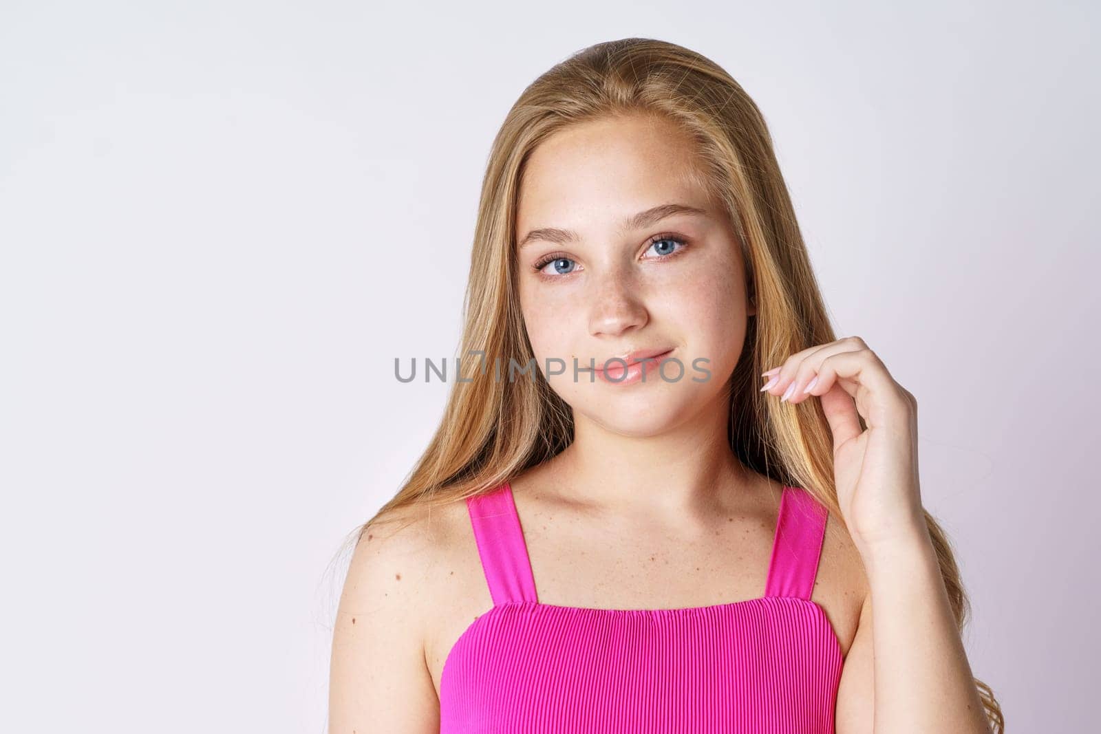 Portrait of a cute girl of blonde Caucasian ethnicity posing on a white background in pink clothes close-up. Happy teenager