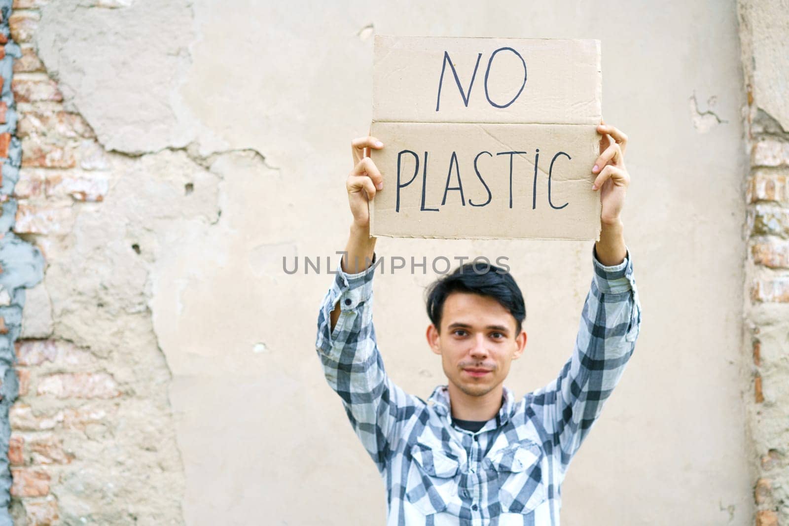 Young man with the inscription on the cardboard no plastic. Caucasian guy at a demonstration against environmental pollution, to help protect the environment. For a clean eco system on the planet