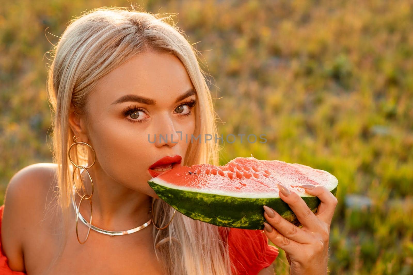 Close-up portrait of a woman biting a watermelon in nature. Beautiful girl of caucasian appearance eats a watermelon on a picnic.