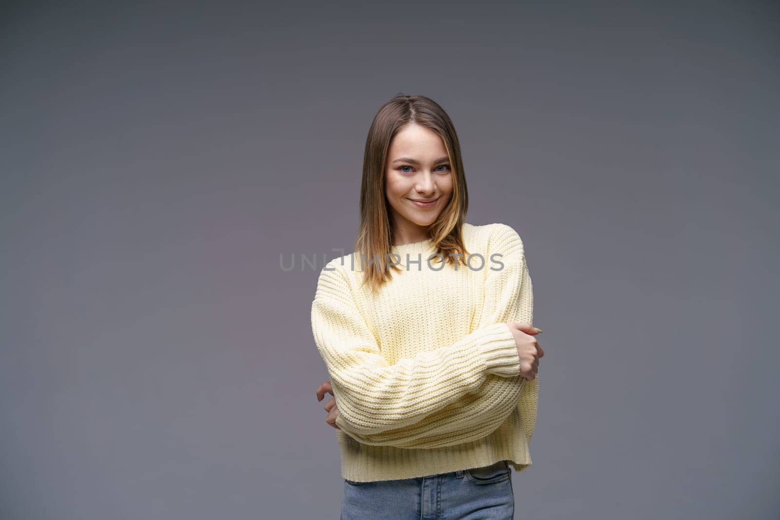 Portrait of a cute young woman of Caucasian ethnicity in a yellow sweater on a gray background looking at the camera. Beautiful confident girl