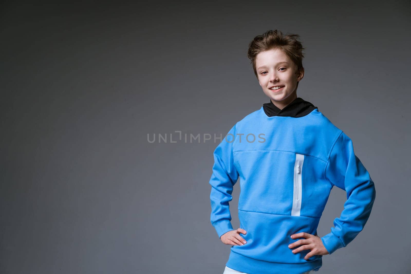 Portrait of a cute guy of European appearance with a snow-white toothy smile in a blue sweatshirt posing on a gray background