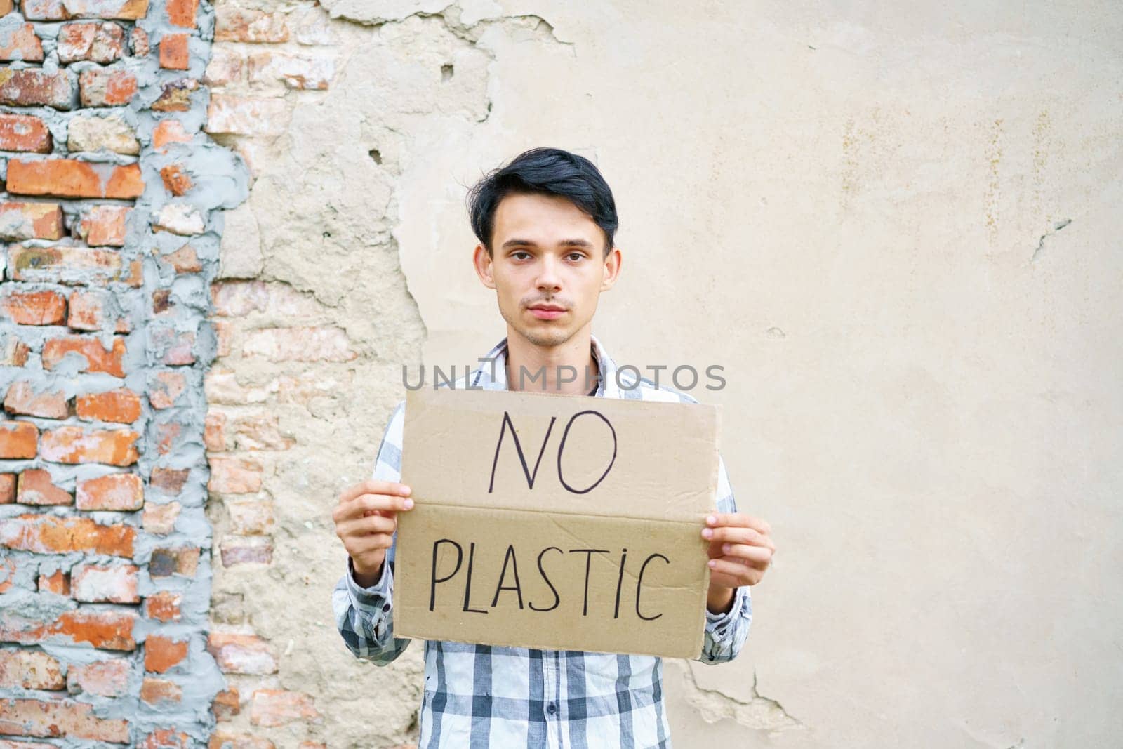 Caucasian guy holding the inscription no plastic. Environmental protection concept from garbage pollution . Young man protesting with placard banning plastic against cement wall background