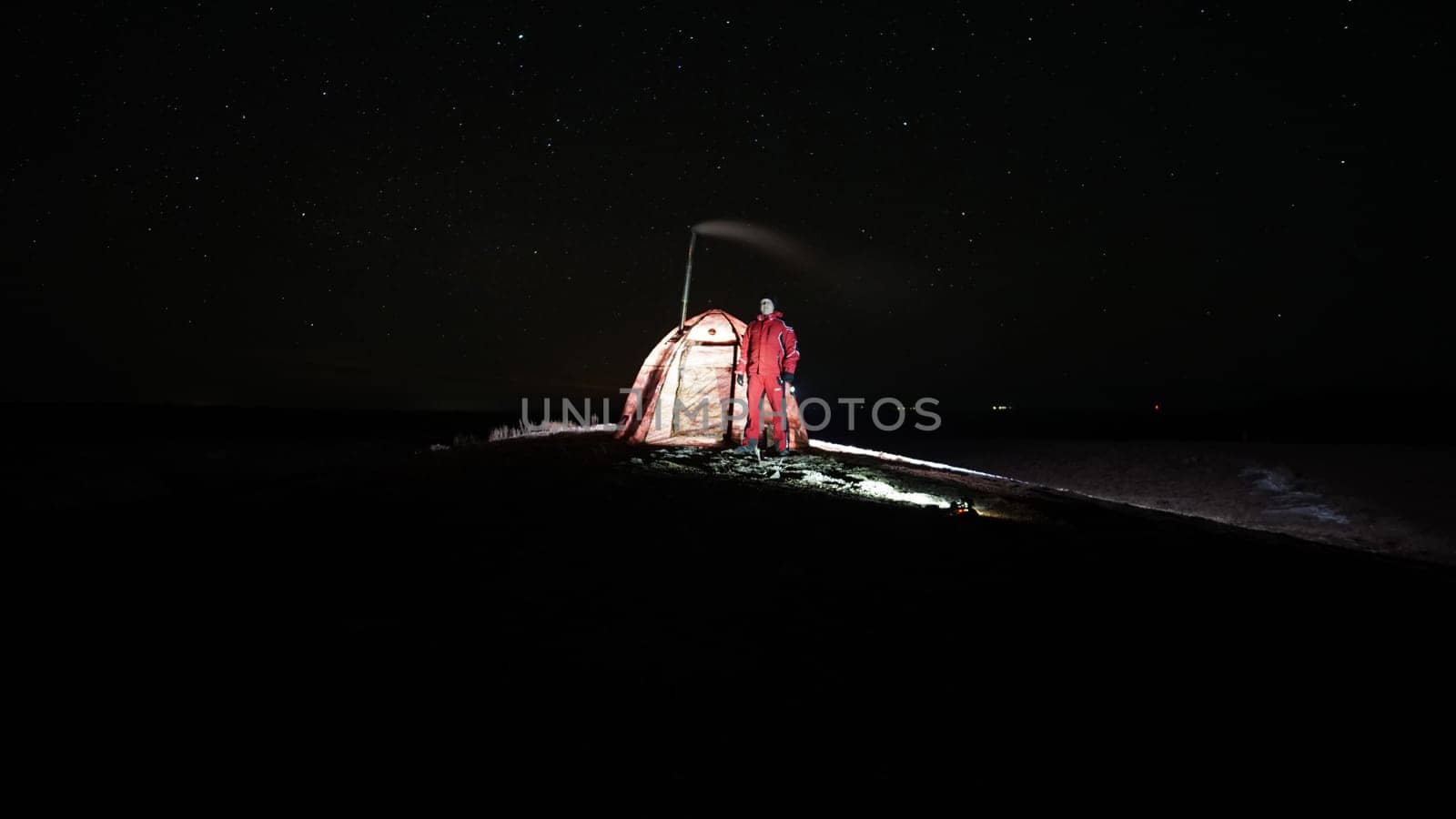 A guy stands near a tent with a stove at night by Passcal