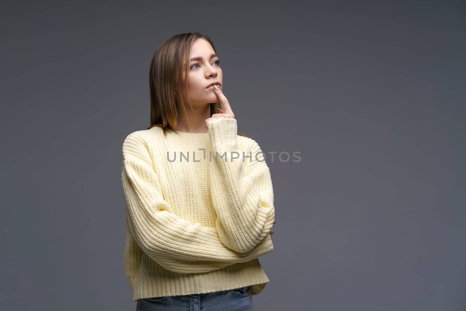 Portrait of sad young woman clenching fists in yellow sweater on gray background by EkaterinaPereslavtseva