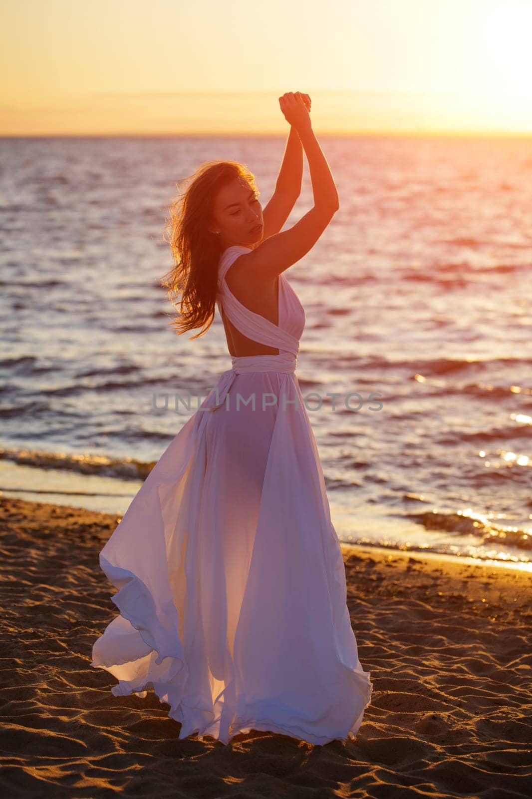 Beautiful woman posing on the beach at sunset in a white dress by EkaterinaPereslavtseva