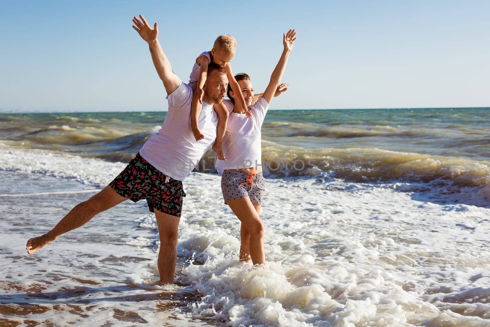 Happy family having fun on summer vacation. Happy son sits on his dad's neck. Cheerful young family on the seashore. Summer holidays for the whole family