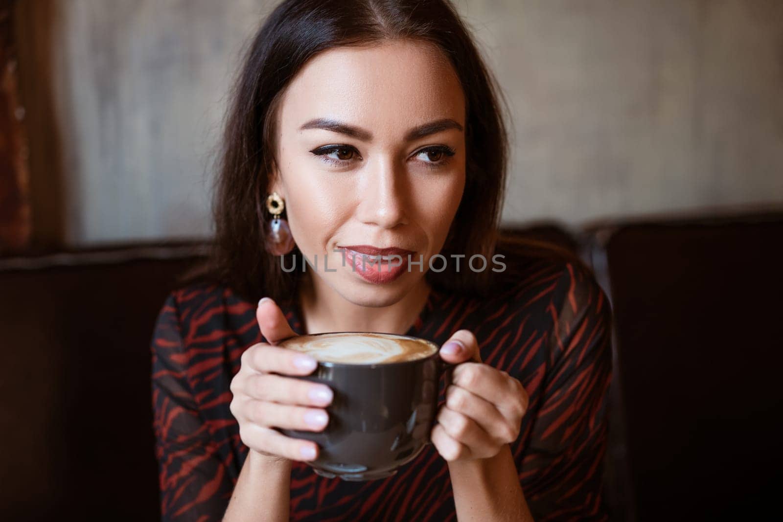 Portrait of a young woman of Caucasian appearance in a cafe with a cup of coffee. Beautiful brunette with brown eyes. Enjoying morning coffee in a cozy cafeteria