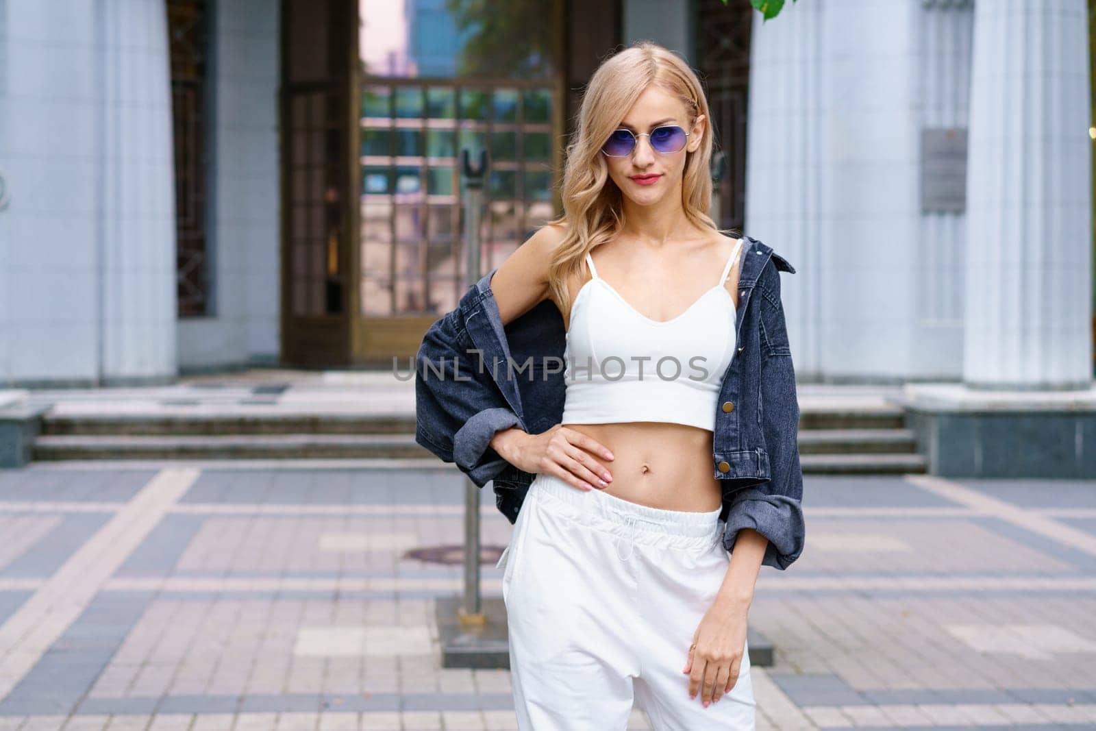 Young woman posing on the street of the city in a tracksuit and sunglasses by EkaterinaPereslavtseva