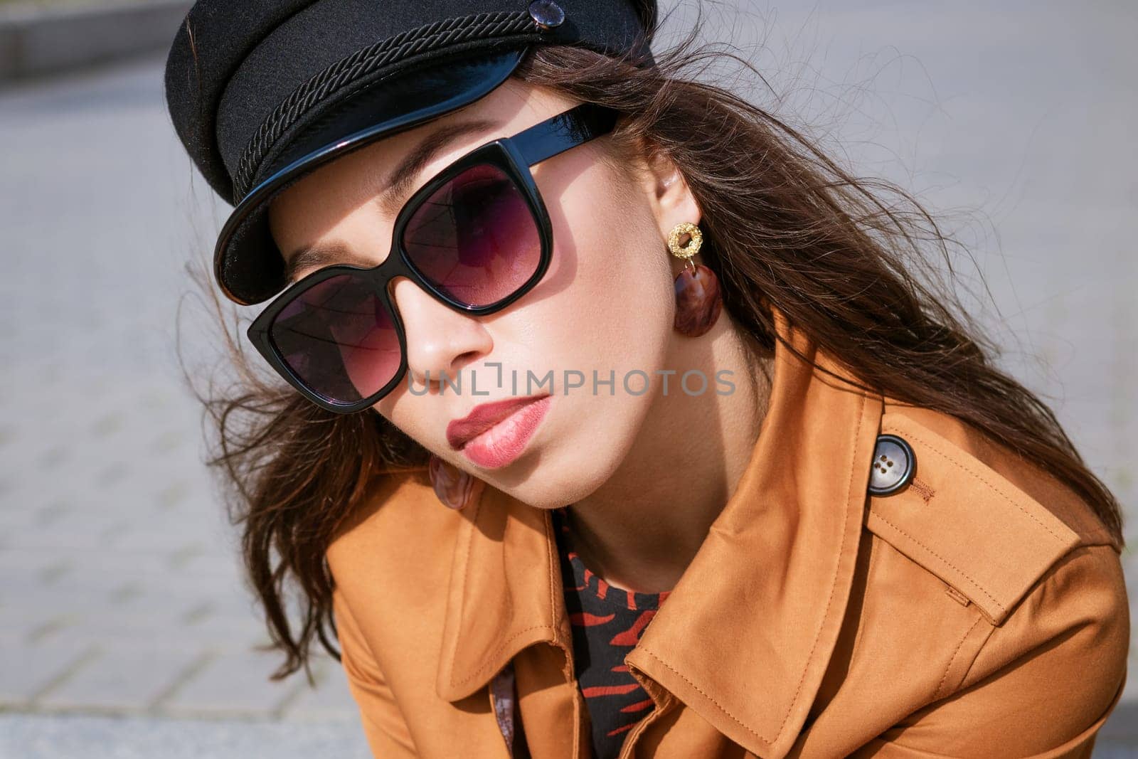 A close-up of a female portre of Caucasian appearance in sunglasses and a black cap looks into the frame. Beautiful brunette woman on a sunny spring day