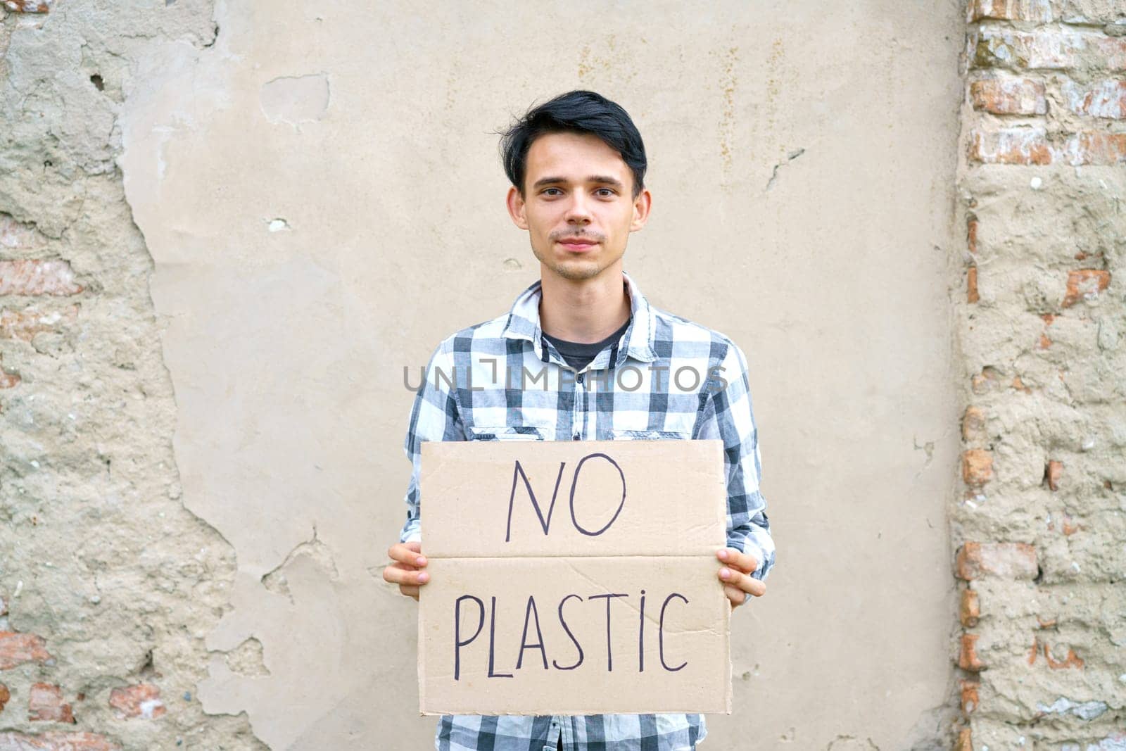 Young man with the inscription on the cardboard no plastic. Caucasian guy at a demonstration against environmental pollution, to help protect the environment. For a clean eco system on the planet