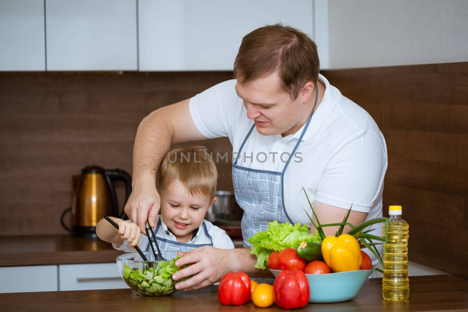 son and father prepare salad together in the kitchen by EkaterinaPereslavtseva