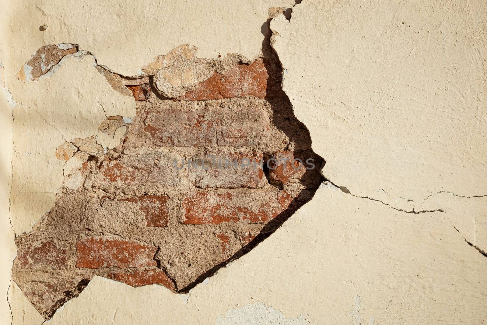 a crack in the beige wall exposing the brickwork