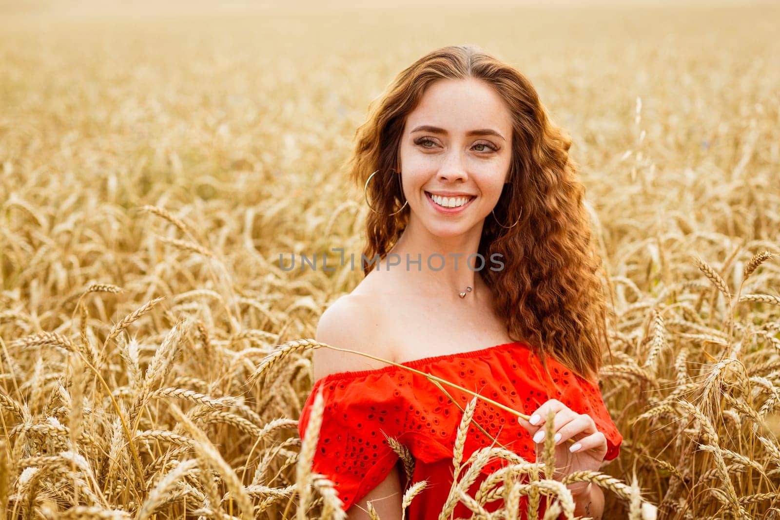 Style redhead young woman in red clothe tay view yellow wheat nature. Cute girl smiles with a snow-white toothy smile. Natural beauty on a natural background. Caucasian real girl.