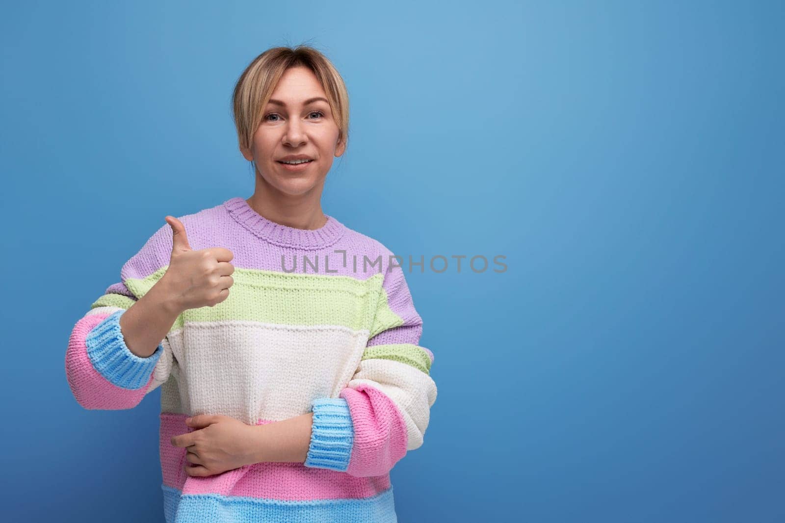 smiling blond woman in casual outfit showing like on blue background with copy space.