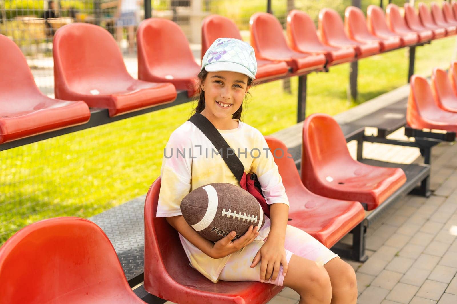 little girl with ball american football in the stadium tribune by Andelov13