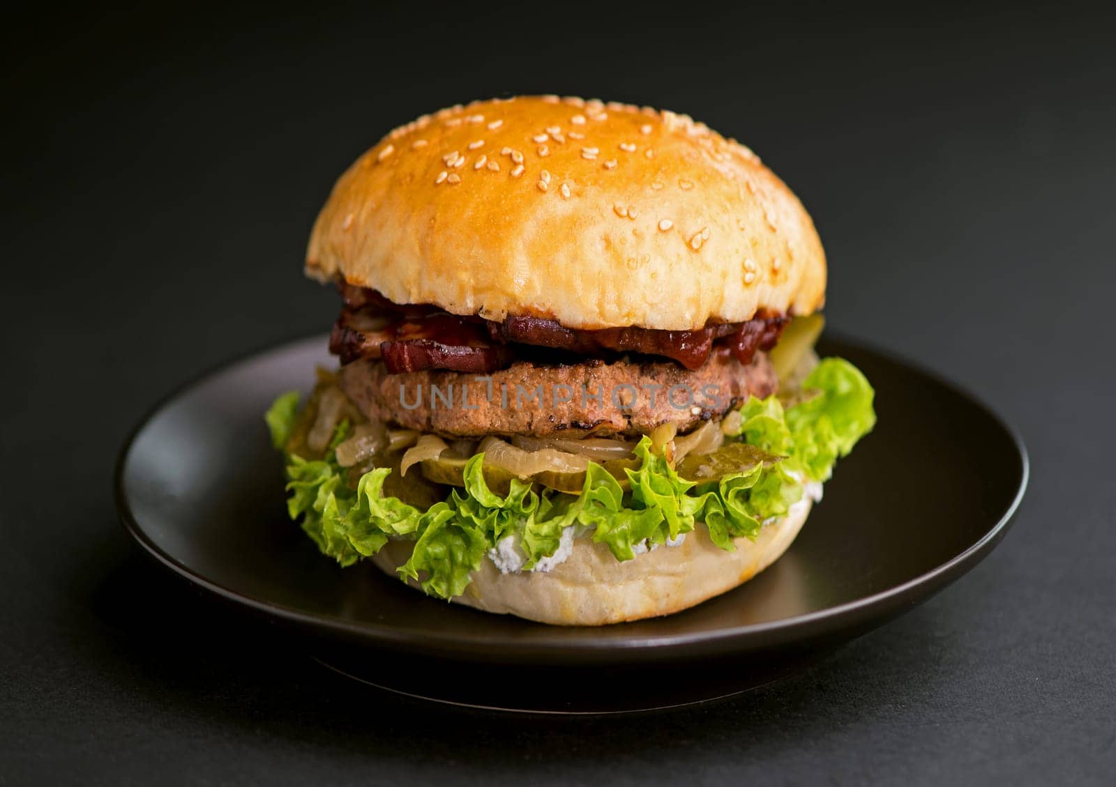 Close-up of a delicious fresh homemade burger with lettuce, onion and tomato on a dark background by aprilphoto