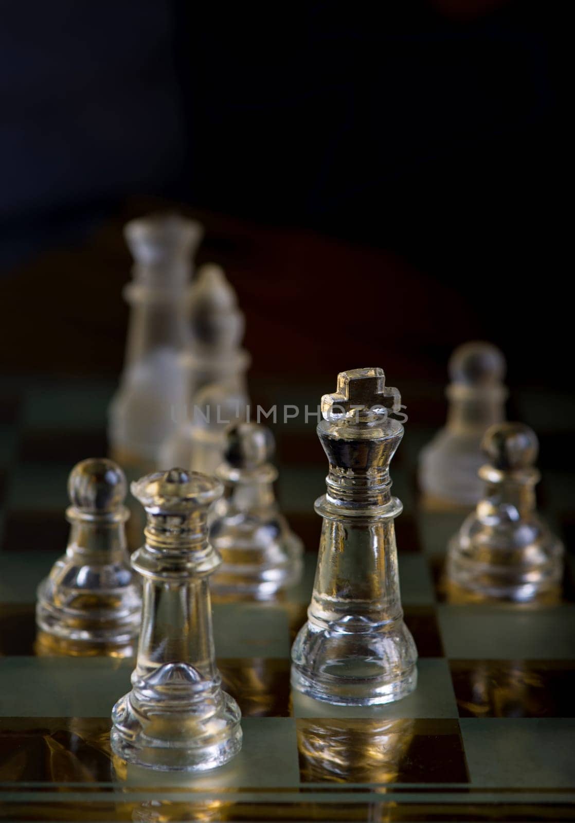 glass chess pieces are defending the king on board in dark by aprilphoto