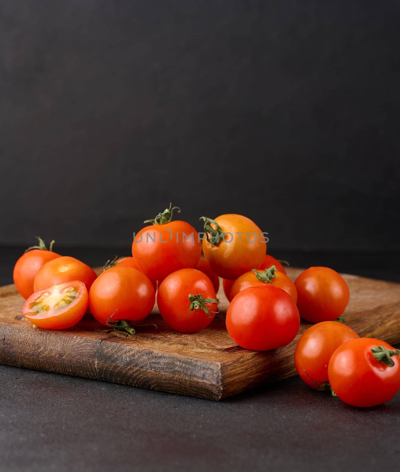 Bunch of ripe red cherry tomatoes on a wooden board, black background by ndanko