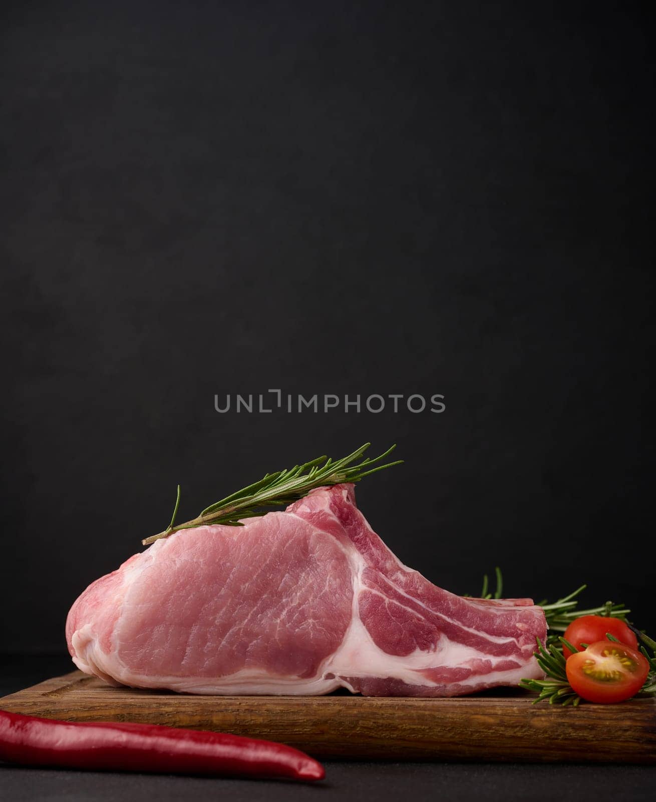 Raw pork tenderloin on the bone and spices on a wooden cutting board on a black background. Portion for lunch and dinner by ndanko