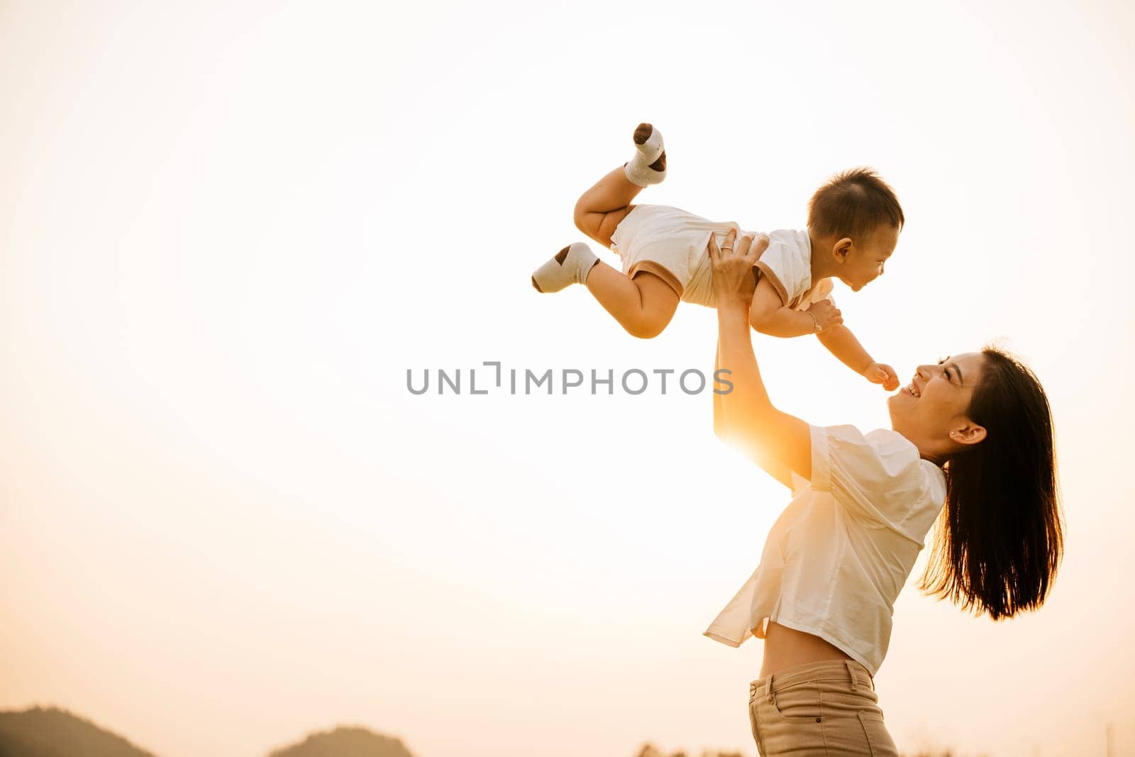 A woman holds her newborn baby up high by Sorapop