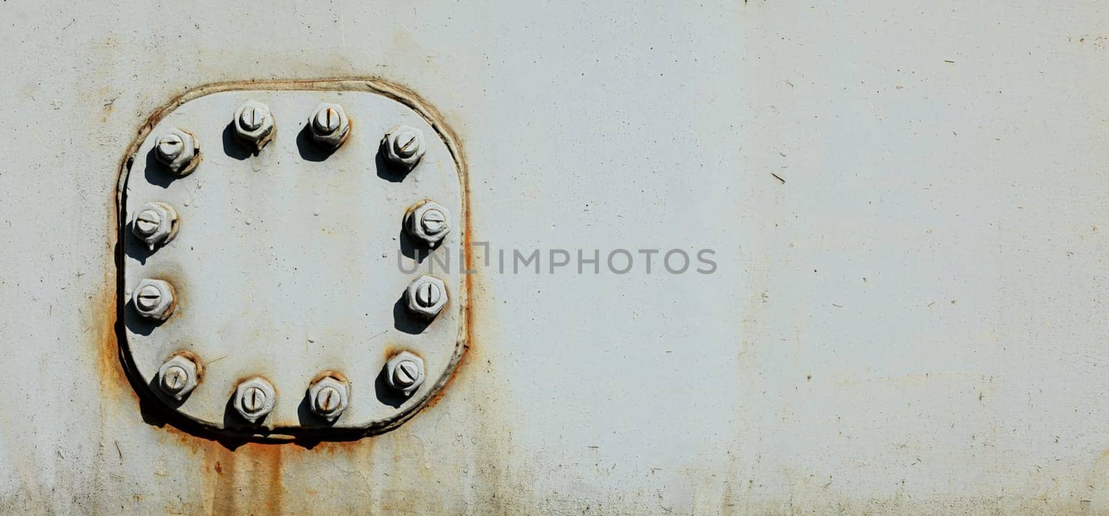 Large nuts and bolts on gray steel plate of rail bridge, lit by bright sun. Abstract industrial background, space for text on the right.
