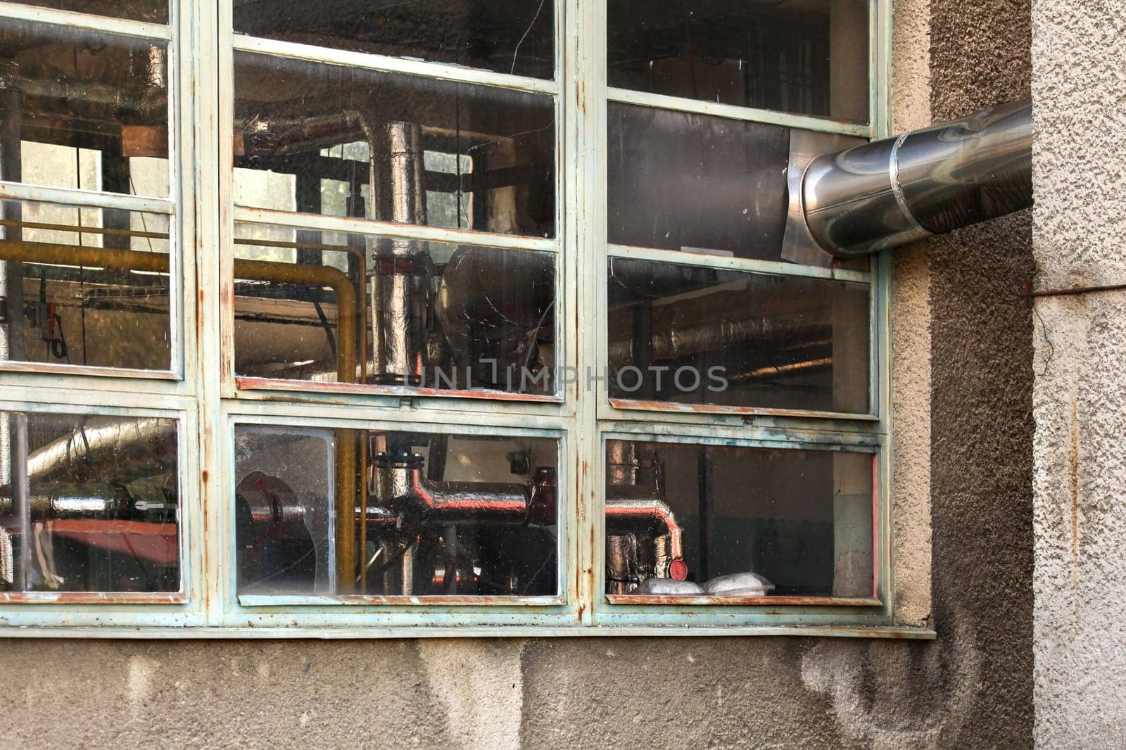 Small old heating plant windows from outside. Heat pipes covered in silver foil visible behind glass.