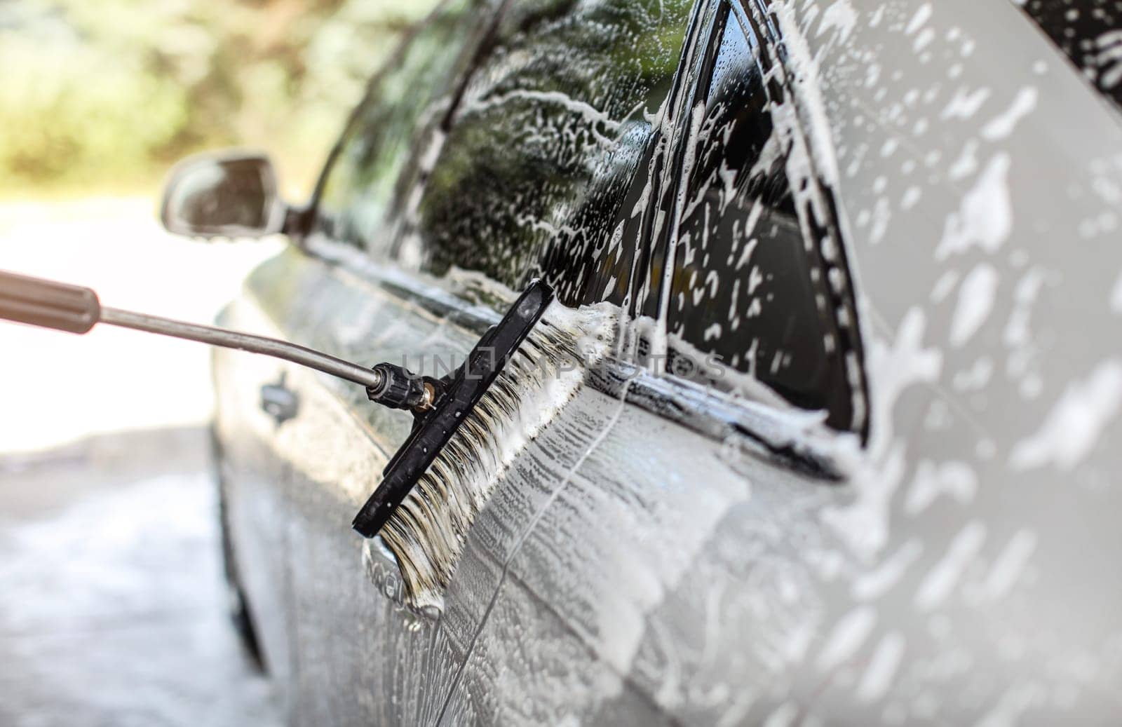 Side of silver car washed in self service manual carwash. Brush leaving strokes in white shampoo foam.