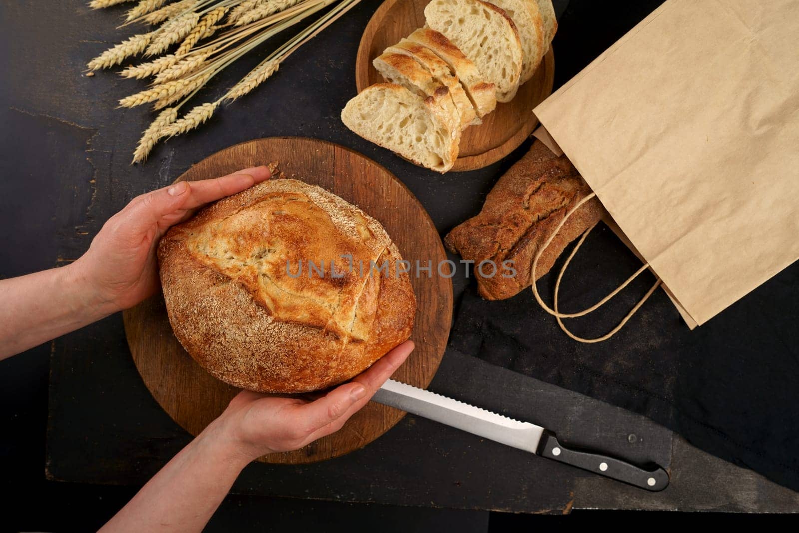 The healthy eating and traditional bakery concept. Top viev. Fresh bread on table close-up. Fresh bread on the kitchen table Whole grain bread put on kitchen wood plate with a chef near knife ready for cut. by aprilphoto