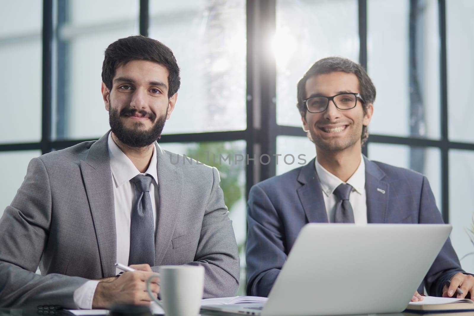 two businessmen are sitting at the table in the office and looking at the camera