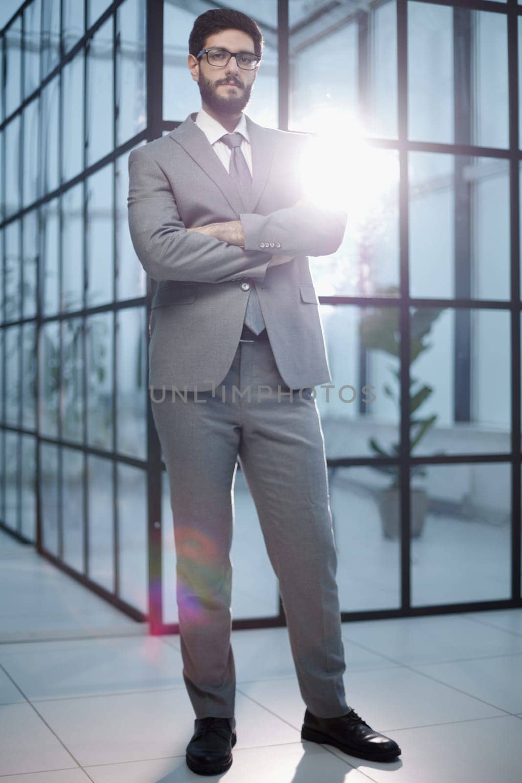 Portrait of young businessman standing in his office with arms crossed by Prosto