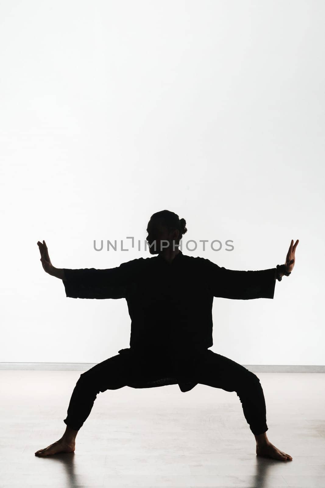 Silhouette of a person practicing qigong energy exercises on a light background.