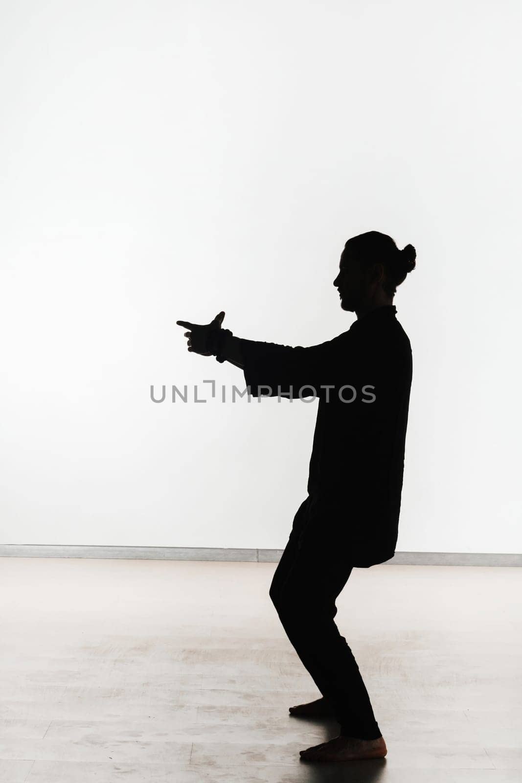 Silhouette of a person practicing qigong energy exercises on a light background.