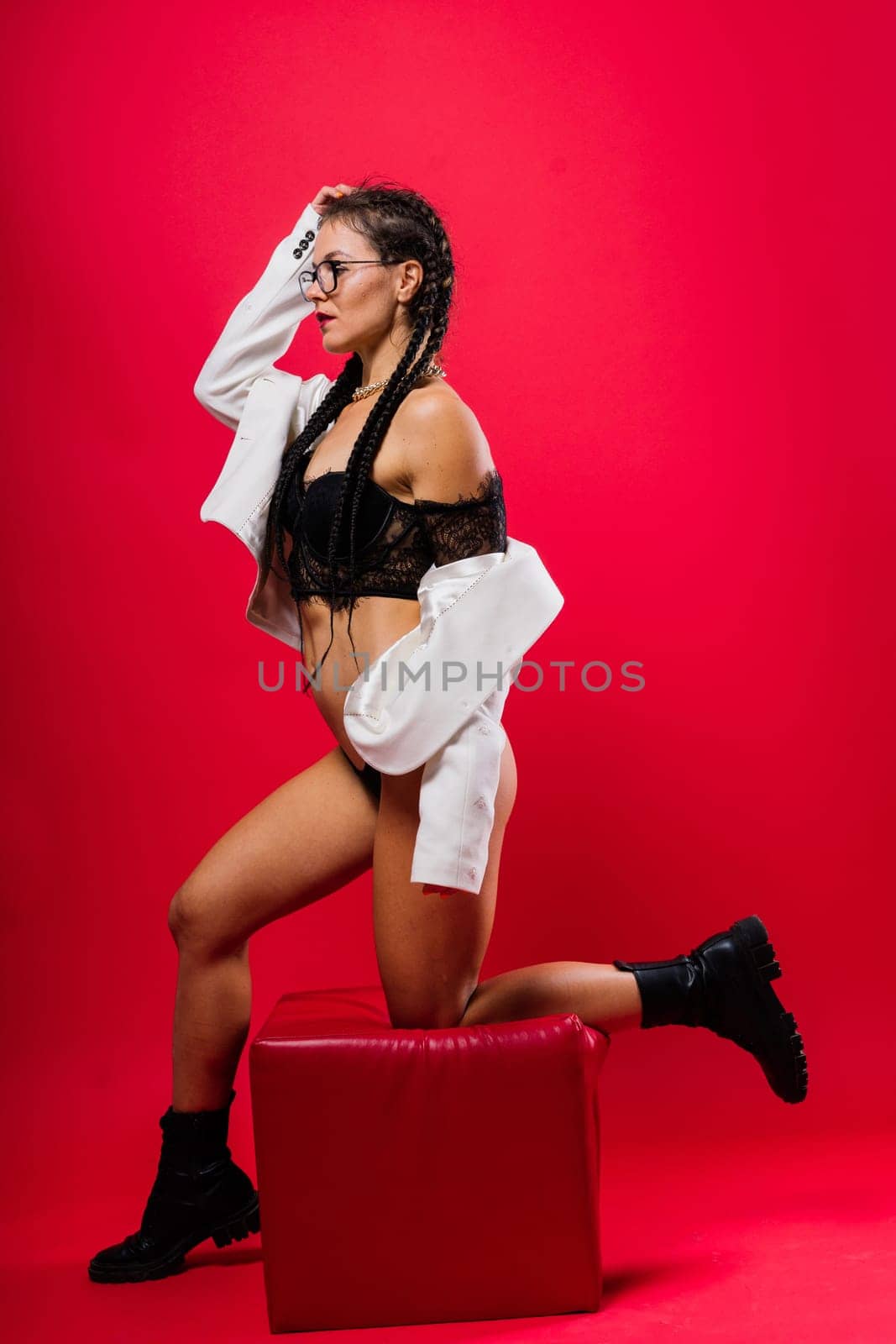 Beautiful female posing in a black underwear and white classic suit over red studio background.