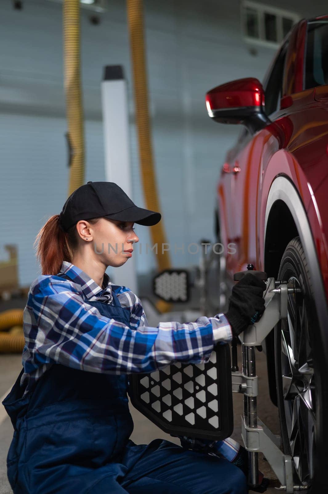 A female auto mechanic makes a camber. Woman working in a car service