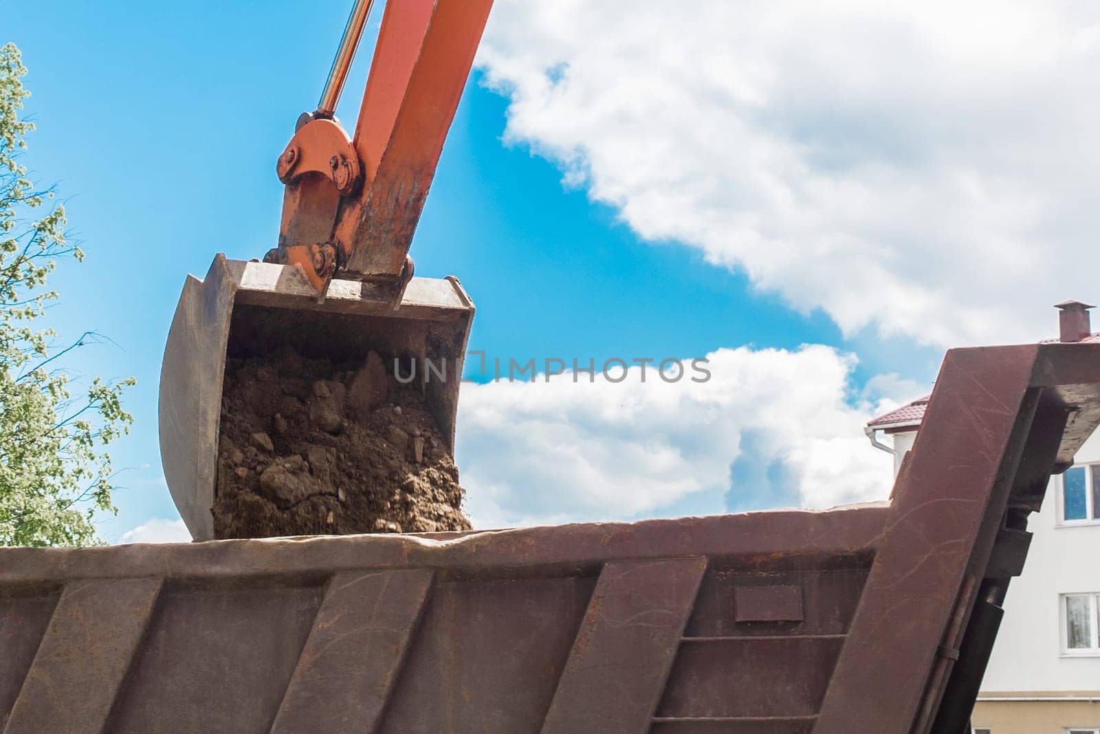 Excavation works. The bucket of the tractor loads the soil with a shovel into the back of a dump truck on the construction site by AYDO8