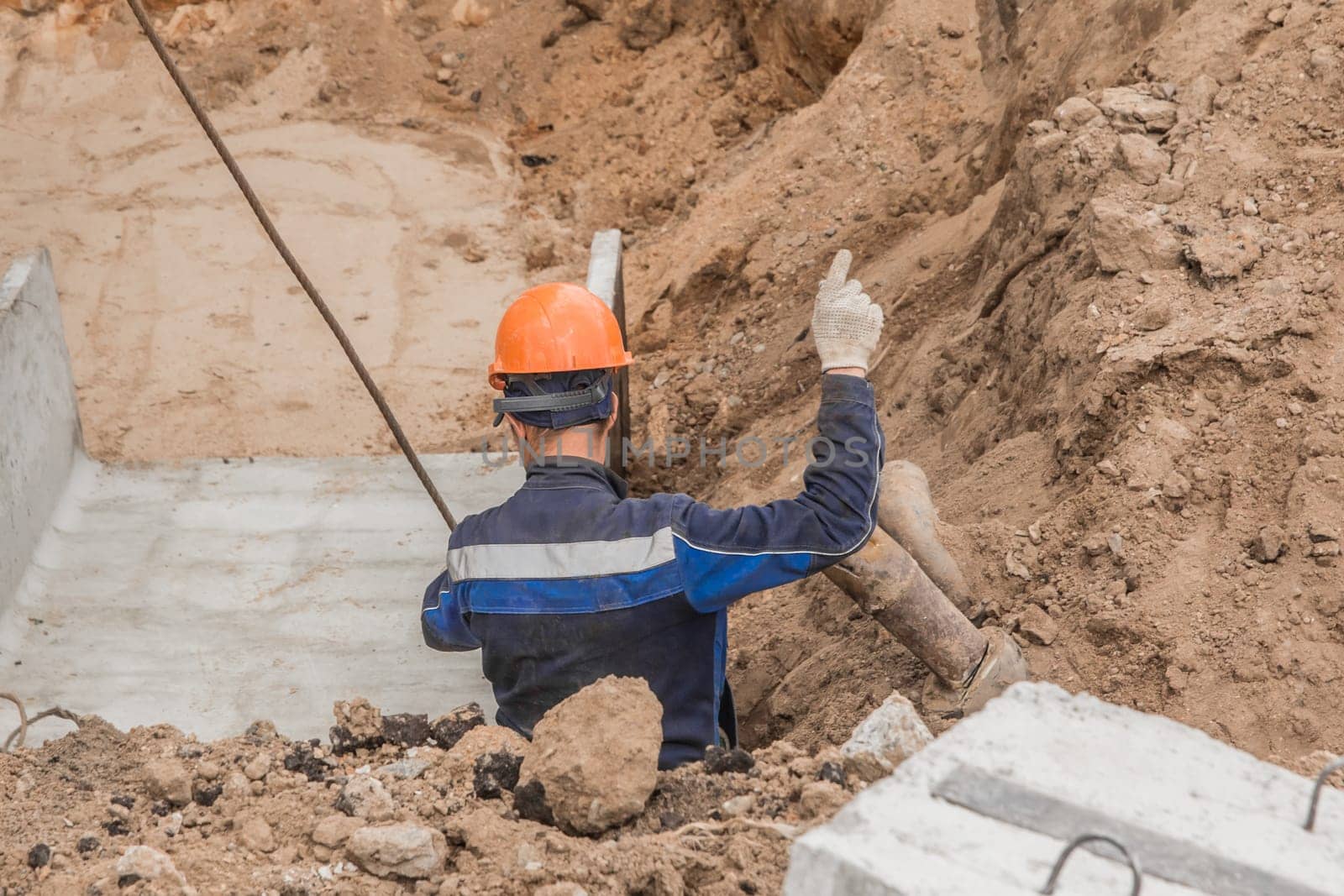 Construction man worker in protective safety helmet and overalls gestures while working in an industrial area of a construction site.