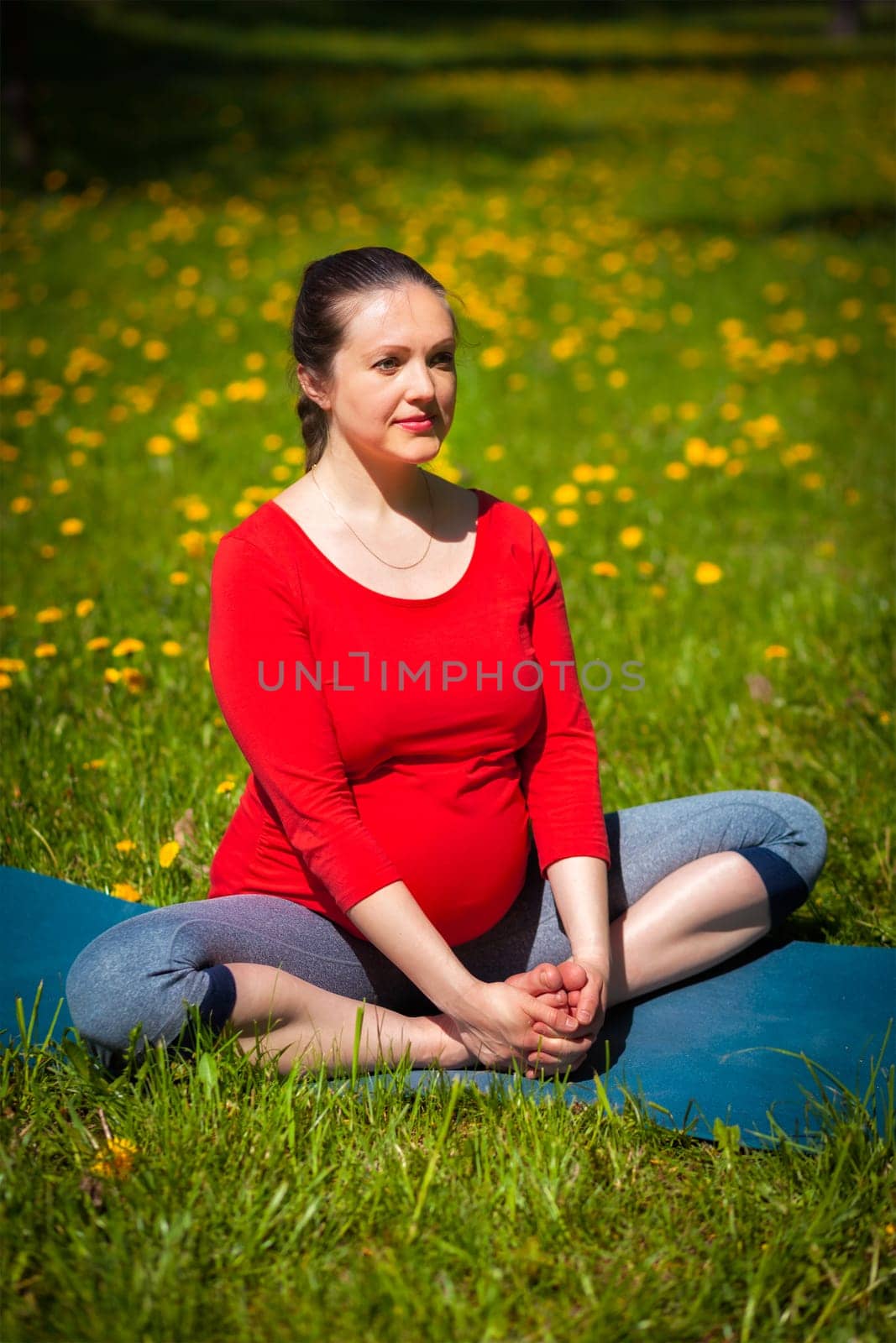 Pregnancy yoga exercise - pregnant woman doing asana baddha konasana bound angle pose outdoors on grass lawn with dandelions in summer