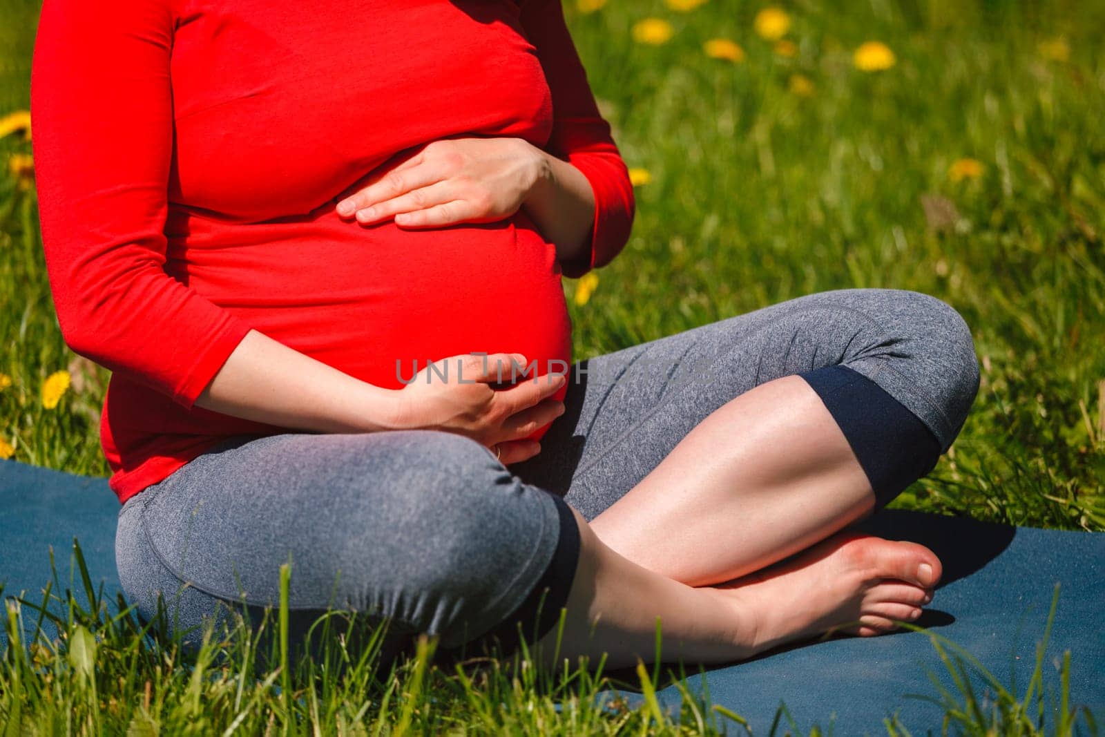 Pregnant woman doing asana Sukhasana outdoors on grass by dimol