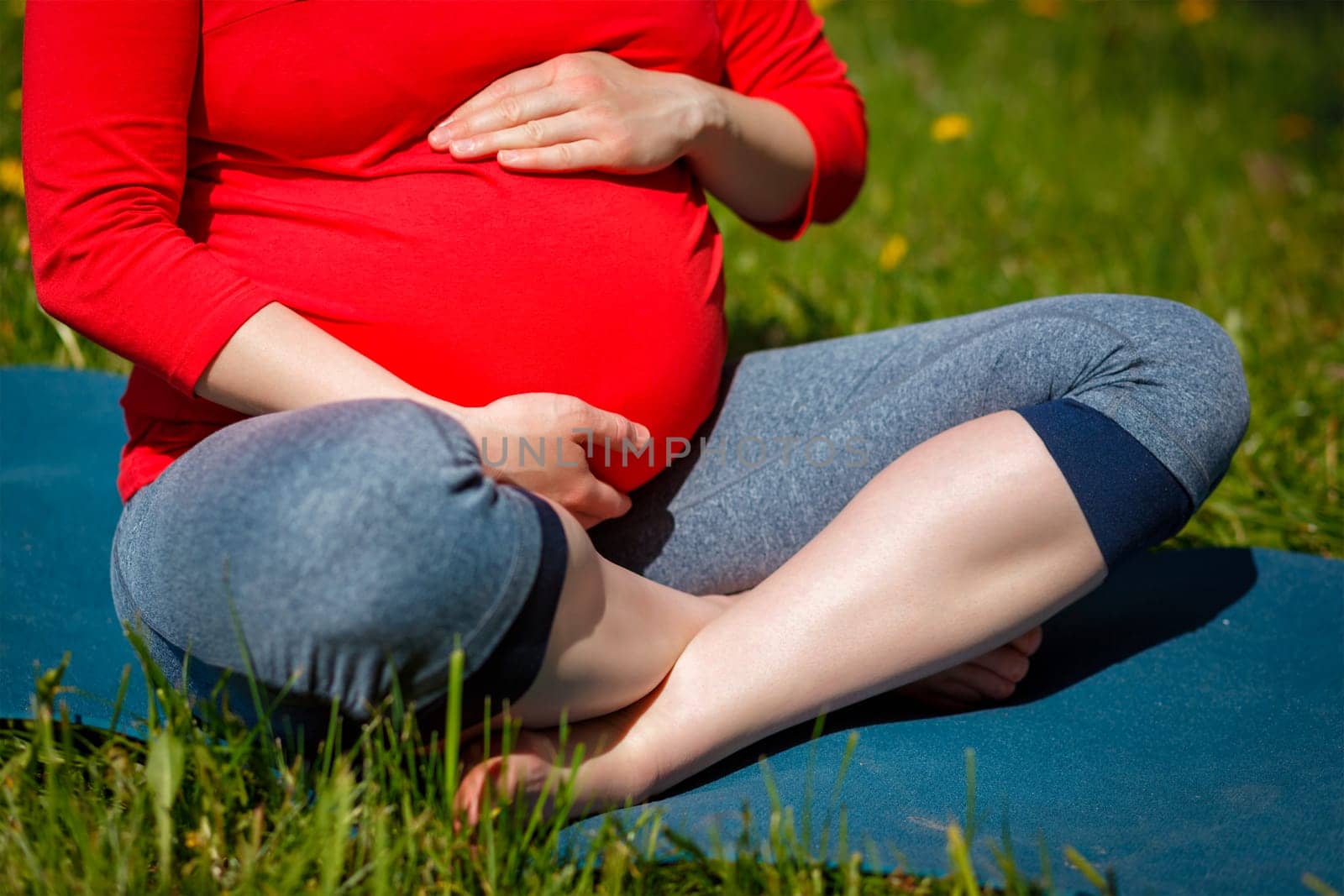 Pregnant woman doing asana Sukhasana outdoors by dimol