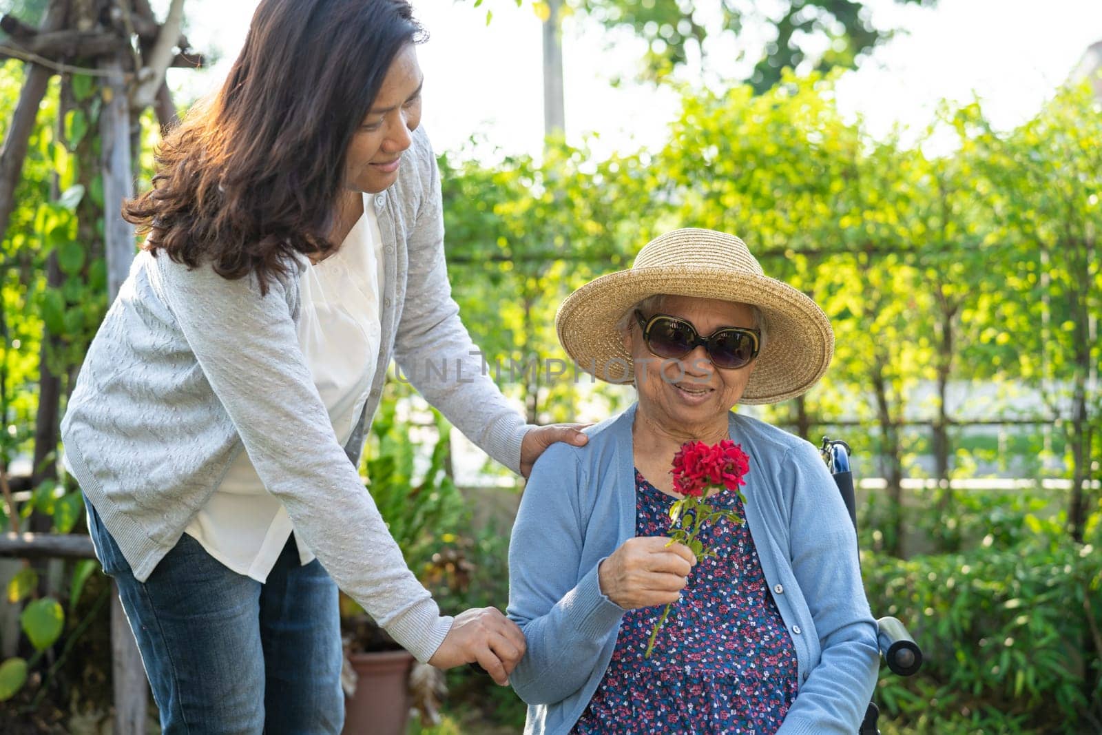Asian senior or elderly old lady woman holding red rose flower, smile and happy in the sunny garden. by pamai