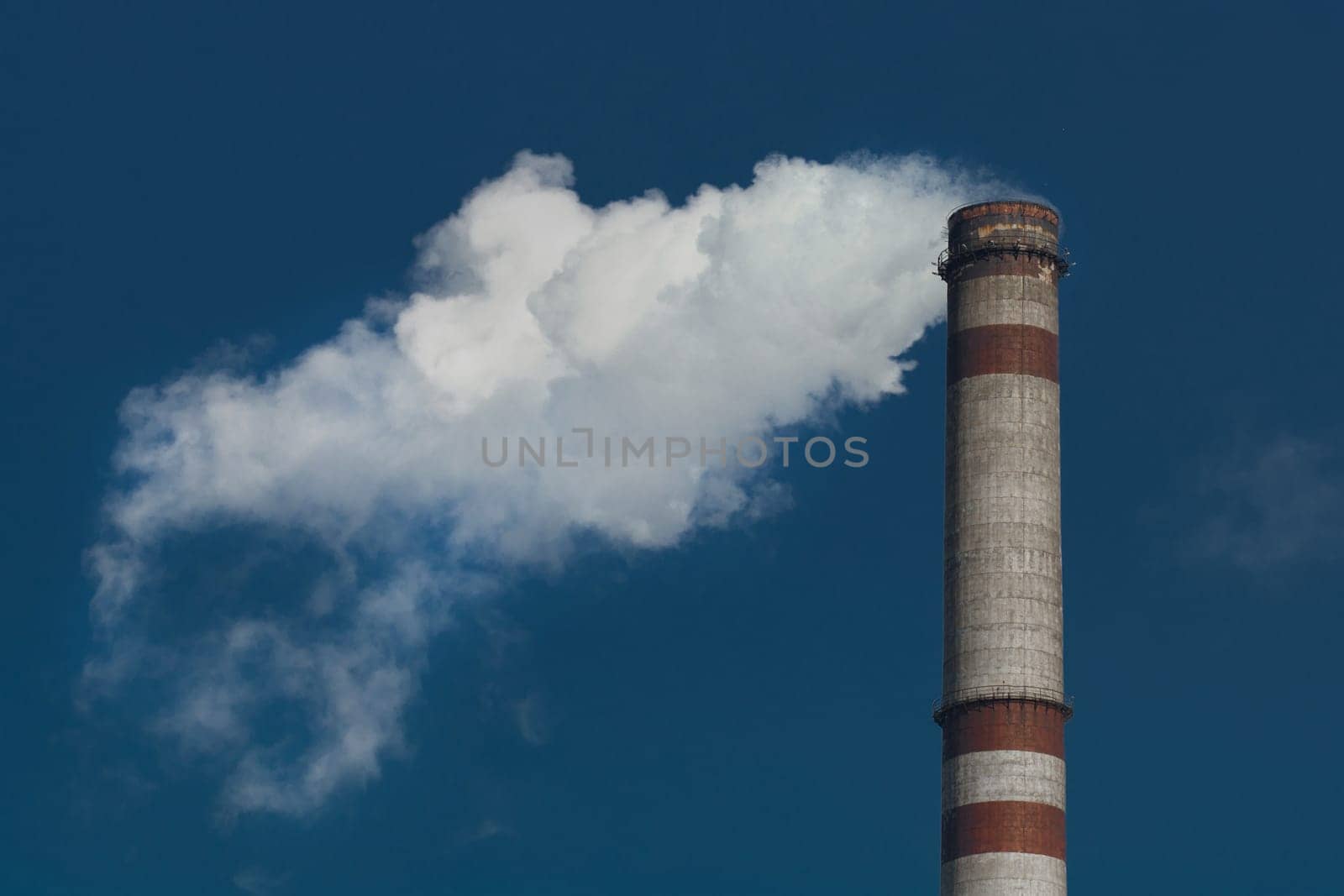 Pollution of the environment, ecology and air. Withdrawal of combustion products of soot, smoke and gases from the pipe of an industrial plant into the atmosphere against the background of a blue sky.