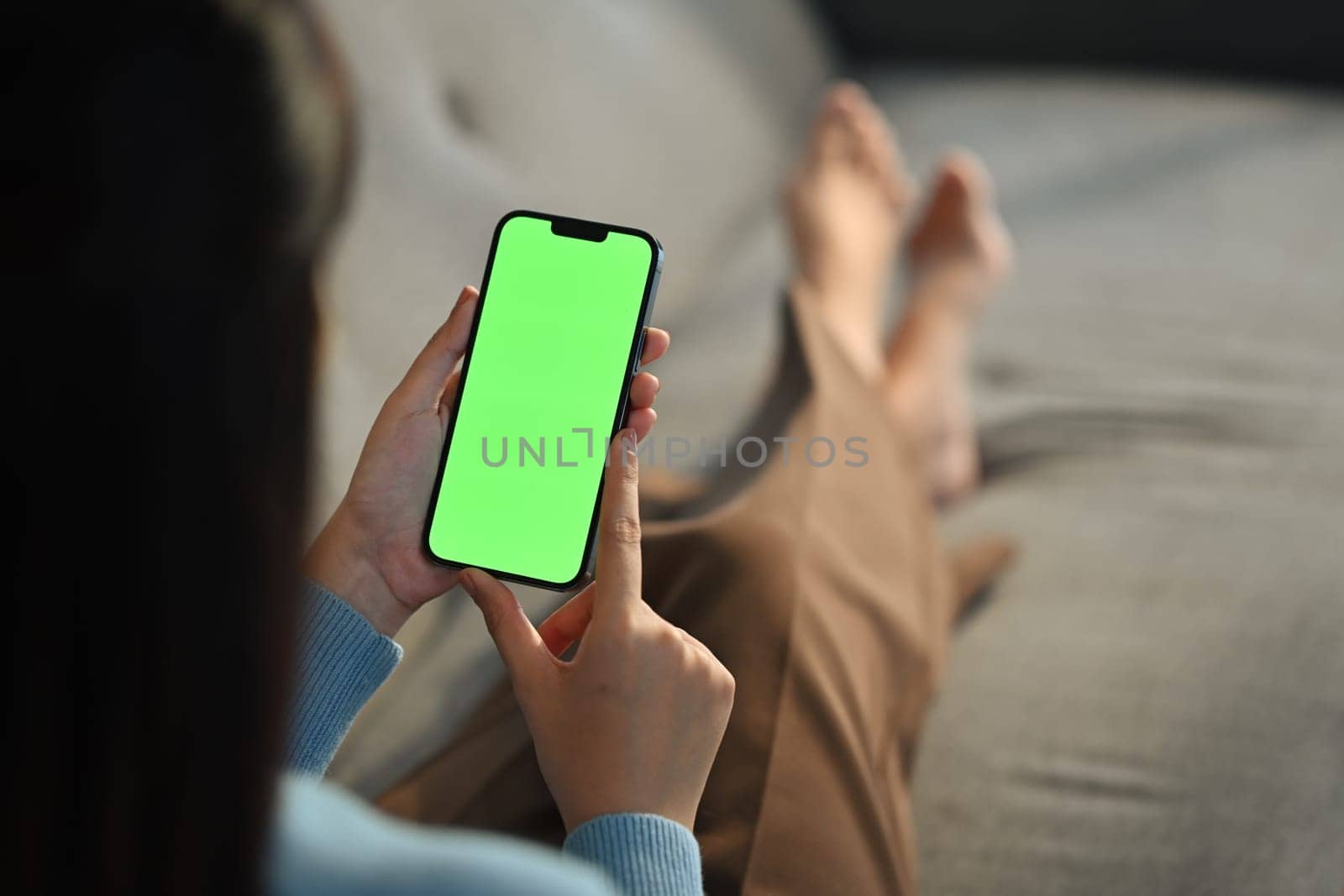 Young woman home use green screen mockup Smartphone, her sitting on sofa in living room. High quality photo