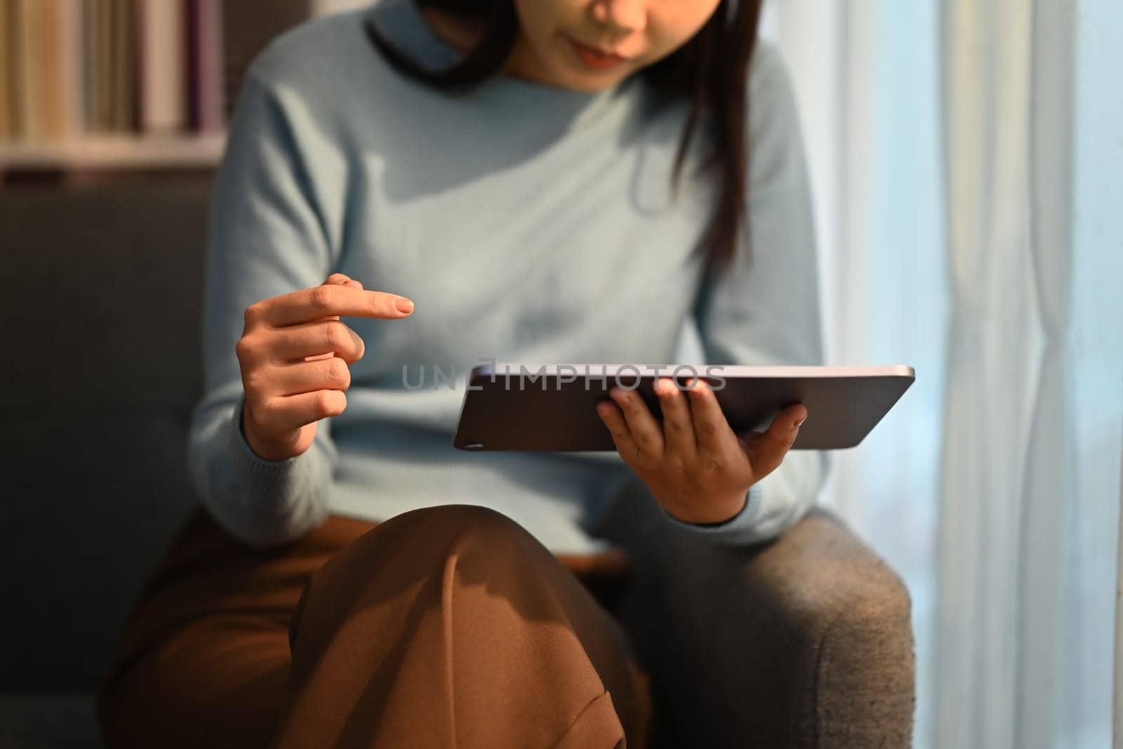 Closeup shot of young woman using her digital tablet while sitting on sofa at home. by prathanchorruangsak