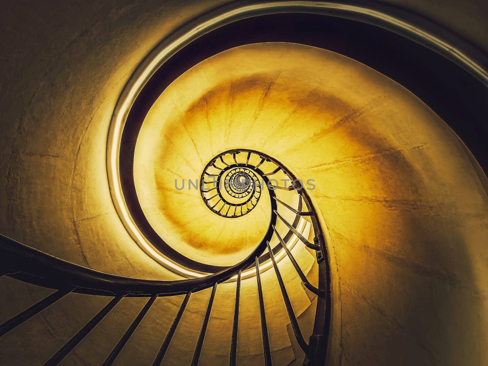 Spiral stairway abstract swirl hypnotising perspective. View downstairs to infinity circular stairs glowing in yellow light background