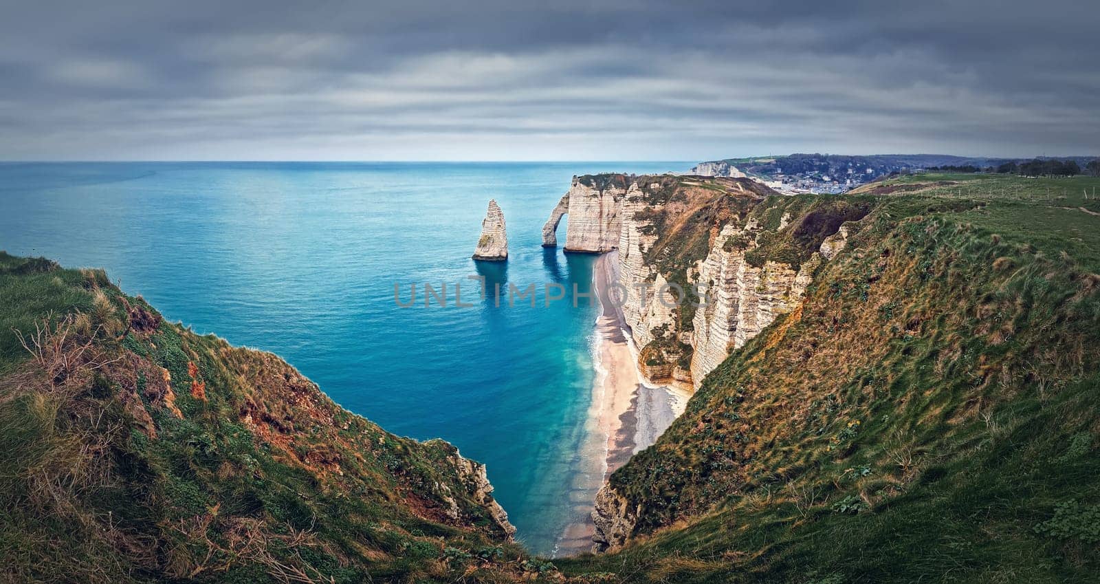 Falaise d'Aval limestone cliffs washed by La Manche channel waters. Beautiful coastline panorama with view to the famous rock Aiguille of Etretat in Normandy, France by psychoshadow