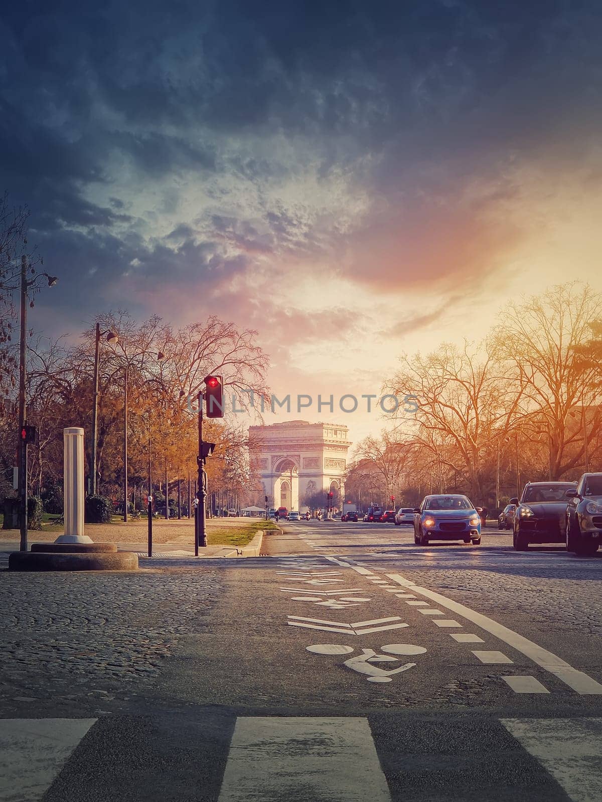 Triumphal Arch (Arc de triomphe) in Paris, France. The famous historic landmark in sunset light seen from the city street with busy traffic