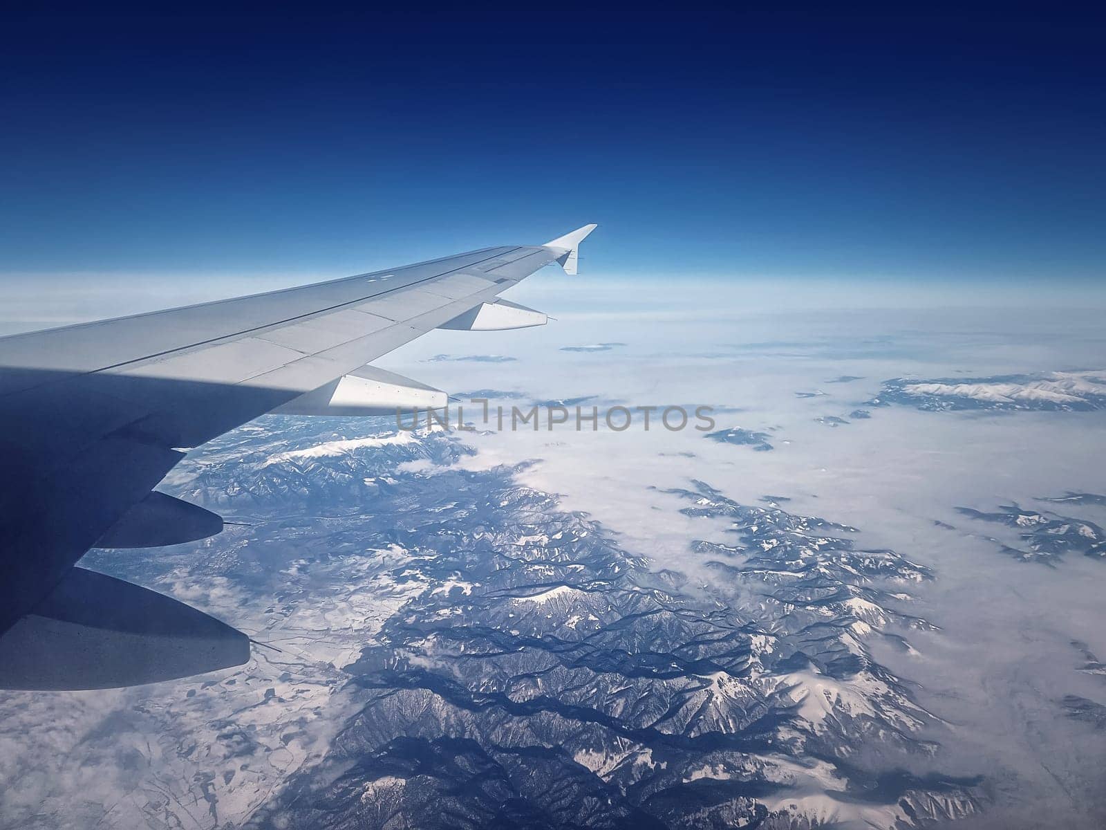 Plane flight above the Carpathian Mountains snowy peaks. Blue skyline and airplane wing seen through the window by psychoshadow