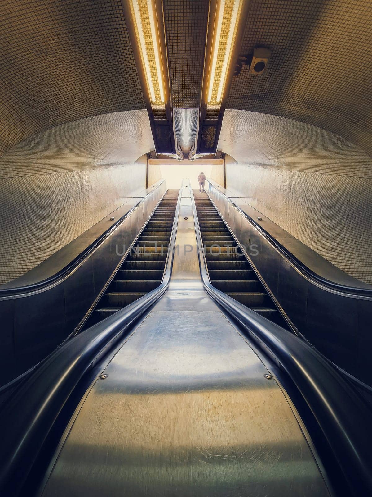 Lone man climbing out on a subway escalator. Symmetrical underground moving staircase by psychoshadow