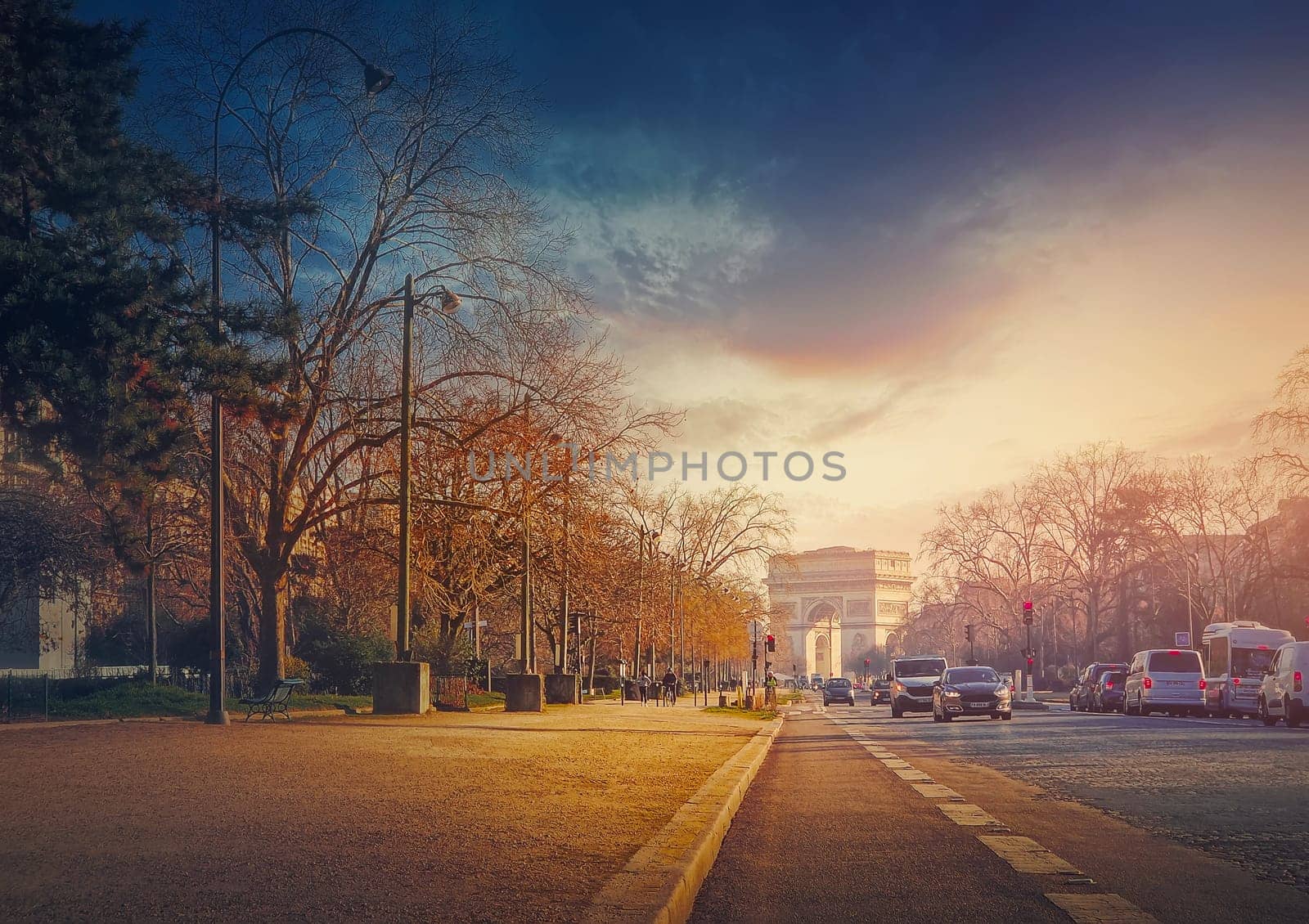 Triumphal Arch (Arc de triomphe) in Paris, France. The famous historic landmark in sunset light seen from the city street with busy traffic