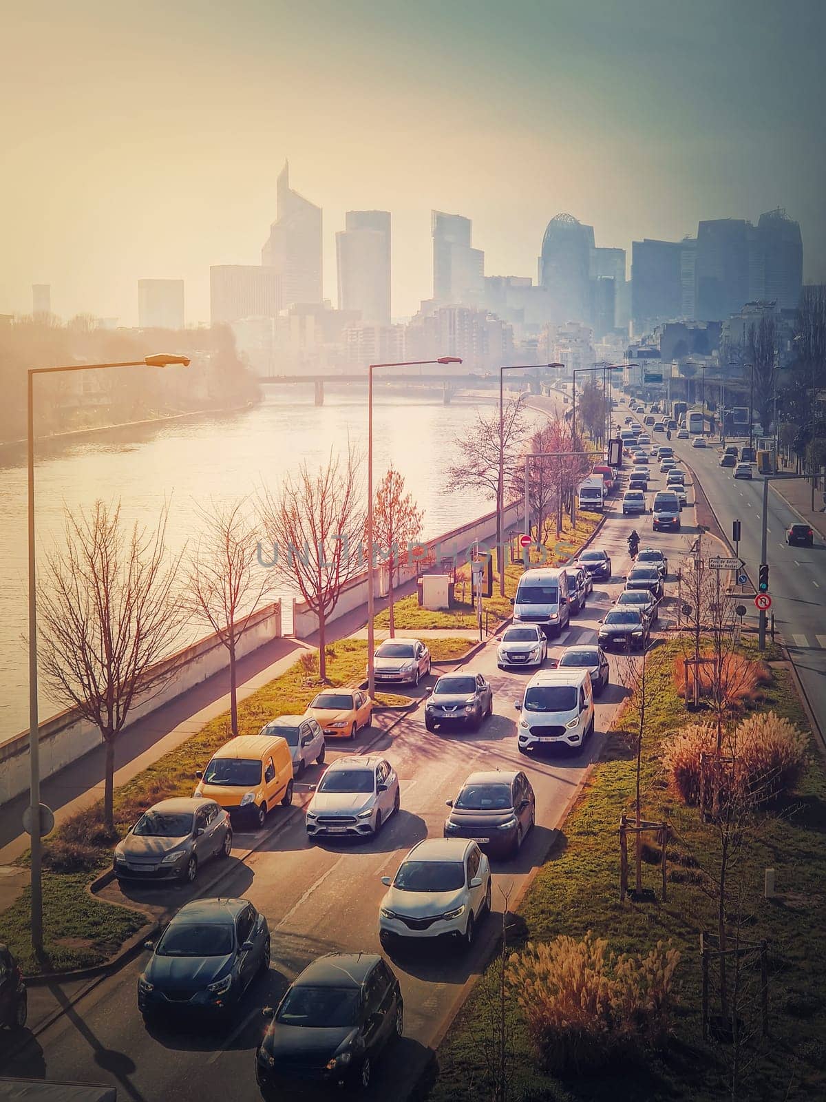 Busy traffic on highway and city streets creating high pollution and smog. Urban sunset view across Seine river to La Defense metropolitan district, Paris, France by psychoshadow